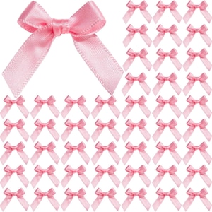 May include: A collection of small, light pink satin ribbon bows arranged in a grid pattern. Each bow features a central knot with two short, angled tails extending downwards, showcasing a smooth, reflective texture and consistent construction.