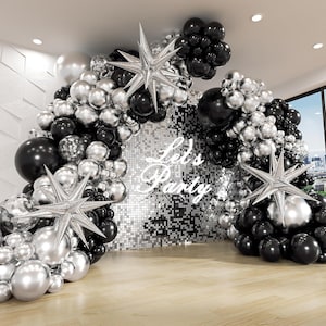 May include: A party decoration featuring a balloon arch in black, silver, and chrome colors. The arch is adorned with star-shaped foil balloons and a backdrop with the text "Let's Party".