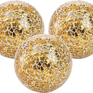 May include: Three decorative spheres with a mosaic design. The spheres are covered in gold-colored, irregularly shaped tiles, creating a textured surface. The mosaic pattern is set against a white background, giving the spheres a bright, reflective appearance.