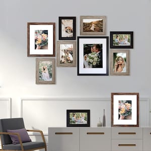 May include: A gallery wall with nine picture frames in various sizes and styles. The frames are arranged in a staggered pattern on a white wall. The frames are all wood and have a rustic finish. Some of the frames are black and some are brown. The frames contain photos of people and landscapes.