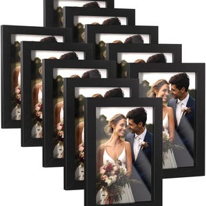 May include: Set of eight black picture frames with a matte finish. Each frame has a clear glass front and a white mat. The frames are arranged in a staggered pattern, with the largest frame in the back and the smallest frame in the front.