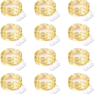 May include: Nine sets of warm white LED string lights, each coiled and paired with a white battery pack. The lights are arranged in a grid pattern, creating a visually appealing display. Ideal for decorative purposes.