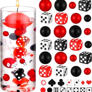 May include: A clear glass cylinder with a floating red candle and dice. The cylinder contains red, black, and gray spheres, red dice, and playing card suit symbols. Additional dice and spheres are arranged around the cylinder.