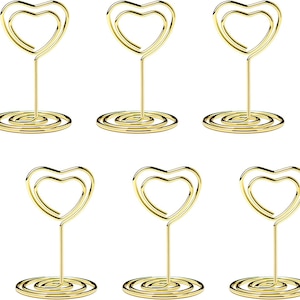 May include: Six gold-colored heart-shaped wire holders. Each holder has a heart-shaped top and a spiral base. The holders are arranged in two rows of three.