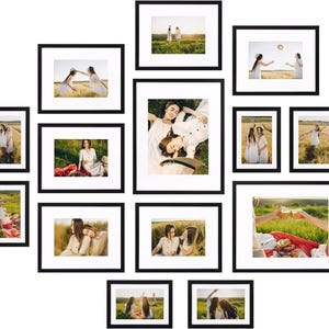 May include: A collection of black framed photographs of people in a field. The photos feature people in white dresses, enjoying a picnic, and throwing a hat in the air. The frames are arranged in a collage.