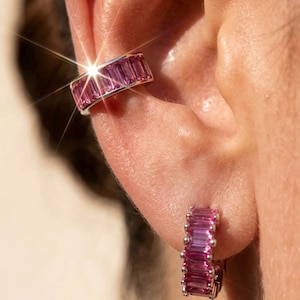 May include: Close-up of a silver ear cuff and hoop earring set. Both pieces feature vibrant pink baguette-cut gemstones. The ear cuff is worn on the upper ear, while the hoop earring is on the earlobe.