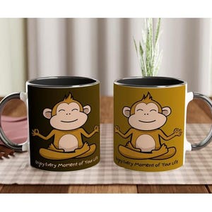Könnte beinhalten: Zwei weiße Keramikbecher mit schwarzen Rändern und Griffen. Jeder Becher zeigt einen Cartoon-Affen in einer Yoga-Pose mit dem Text "Enjoy Every Moment of Your Life".
