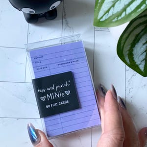 May include: A clear plastic case containing a stack of 60 flat cards with a lavender background. A black label reads "kiss and punch MINIs" with a heart symbol. The cards have lines for "Author," "Title," and "Borrower's Name."