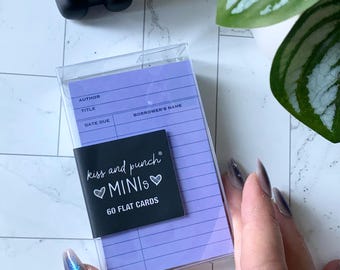 May include: A clear plastic case containing a stack of 60 flat cards with a lavender background. A black label reads "kiss and punch MINIs" with a heart symbol. The cards have lines for "Author," "Title," and "Borrower's Name."