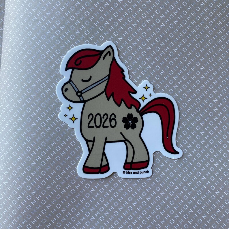 May include: A sticker depicting a cartoon pony with a tan body, red mane and tail, and a bridle. The pony has the number "2026" and a black flower on its side. The sticker has a white border and the text "Kiss and punch".