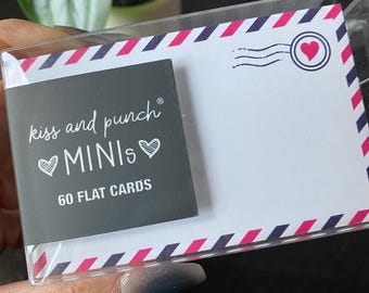 May include: A clear plastic case holding a set of flat cards. The cards have a white background with a pink and navy blue border. A small black card with the text "kiss and punch MINIs" and "60 FLAT CARDS" is visible.