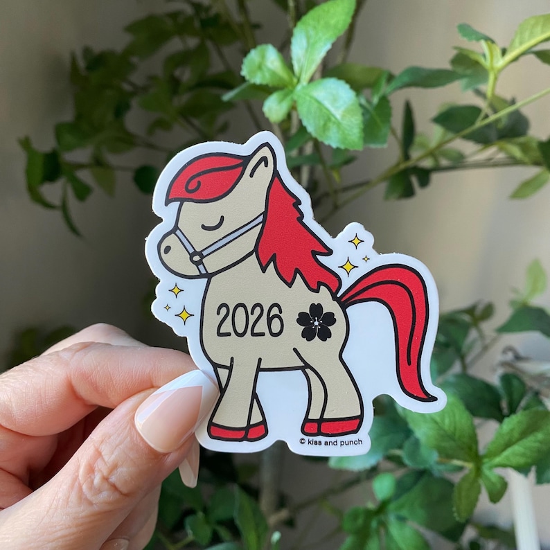 May include: A sticker depicting a cartoon horse with a red mane and tail, wearing a bridle. The number "2026" is on the horse's body, alongside a four-leaf clover. The sticker has a white border and the text "Kiss and Punch".