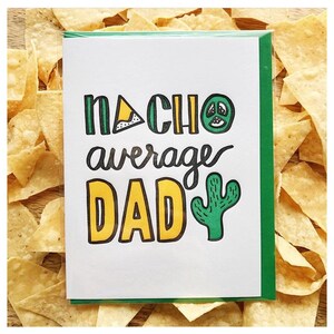 May include: A white card with the text "NACHO average DAD" in green and yellow, featuring a peace sign and cactus illustration. The card has a green border and is surrounded by tortilla chips.