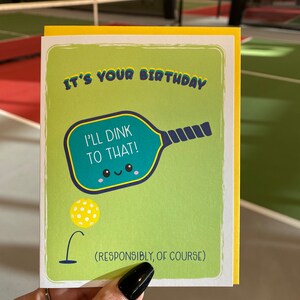 May include: A yellow and green birthday card with a cartoon pickleball paddle and the text "It's your birthday. I'll Dink to that! (Responsibly, of course)"