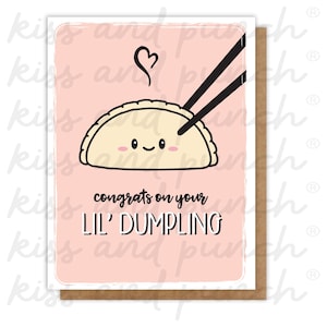 May include: A greeting card with a light pink background and a cartoon dumpling design. The dumpling is being held by black chopsticks, with a heart above it. The text reads "congrats on your lil' DUMPLING".
