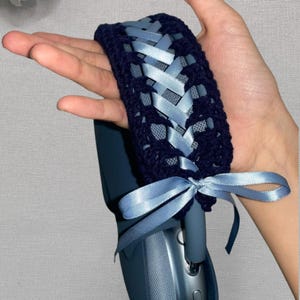 May include: Navy blue crochet headphone cover with light blue satin ribbon woven through the design. The cover is tied with a bow. The headphones are a matching navy blue color.
