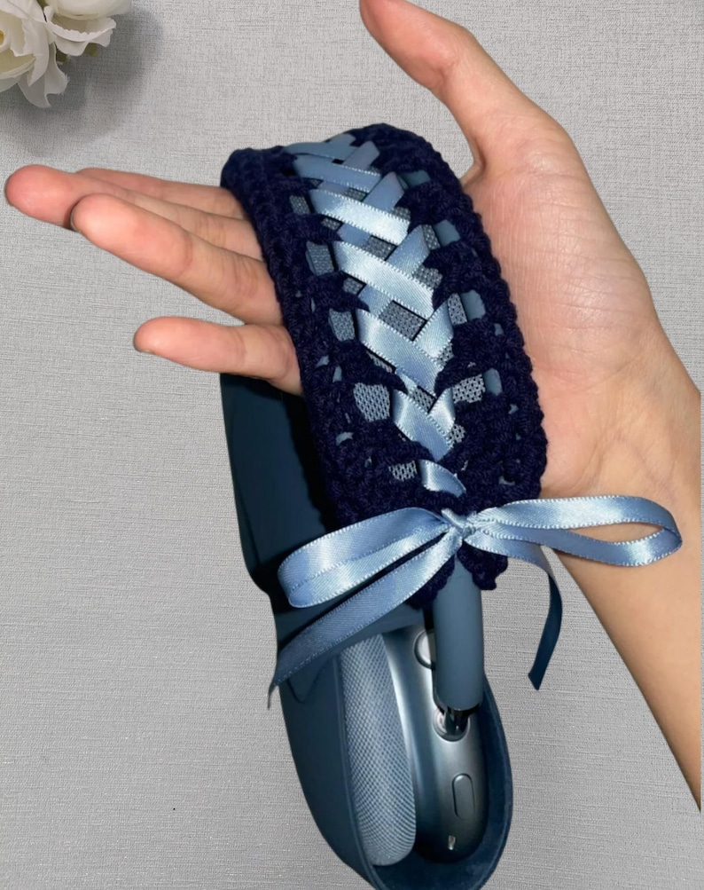 May include: Navy blue crochet headphone cover with light blue satin ribbon woven through the design. The cover is tied with a bow. The headphones are a matching navy blue color.