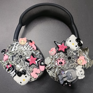 K&ouml;nnte beinhalten: Schwarzer Kopfh&ouml;rer, verziert mit verschiedenen Charms, darunter Hello Kitty, Sterne, Schleifen und das Wort "Barbie". Die Charms sind in Rosa, Silber und Wei&szlig; gehalten und schaffen ein verspieltes und dekoratives Design.