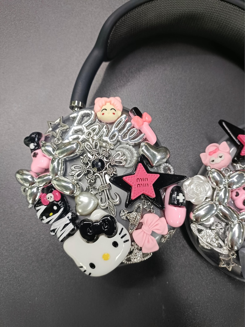 K&ouml;nnte beinhalten: Schwarzer Kopfh&ouml;rer, verziert mit dekorativen Charms, darunter ein Hello Kitty-Design, rosa Schleifen und das Wort "Barbie" in silberner Schrift. Das Design beinhaltet Sterne, Herzen und andere Verzierungen.