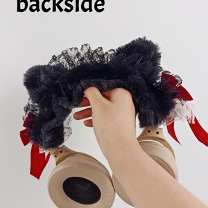 May include: Black faux fur headphone cover with black lace trim and red satin bows. The text "backside" is printed in black at the top. The headphones are tan.