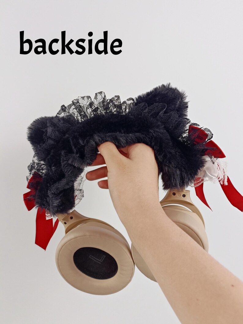 May include: Black faux fur headphone cover with black lace trim and red satin bows. The text "backside" is printed in black at the top. The headphones are tan.