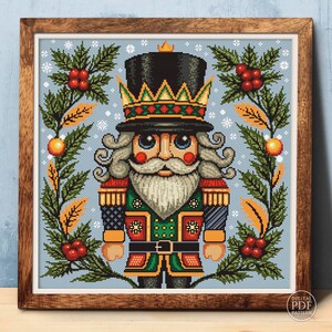 May include: A cross-stitch pattern featuring a colorful nutcracker with a crown, holding a staff and standing in front of a wintery background with holly and snowflakes.