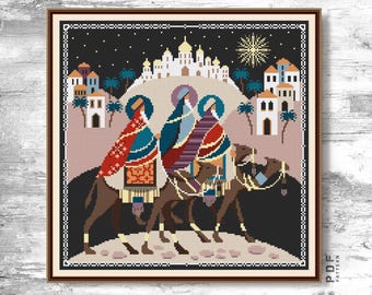 Peut inclure: Une broderie au point de croix encadrée représentant les trois rois mages sur des chameaux, se dirigeant vers une ville sous un ciel étoilé. L'œuvre utilise des rouges, des bleus et des bruns, avec une étoile en haut à droite.