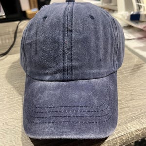 May include: A dark blue denim baseball cap with a slightly distressed look. The cap has a curved brim and a structured crown.