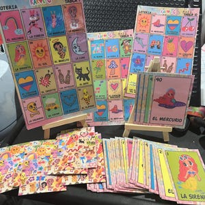 May include: A set of colorful playing cards with illustrations of various characters and objects. The cards are arranged in a grid pattern and feature the text "KAROL G" and "LOTERIA".