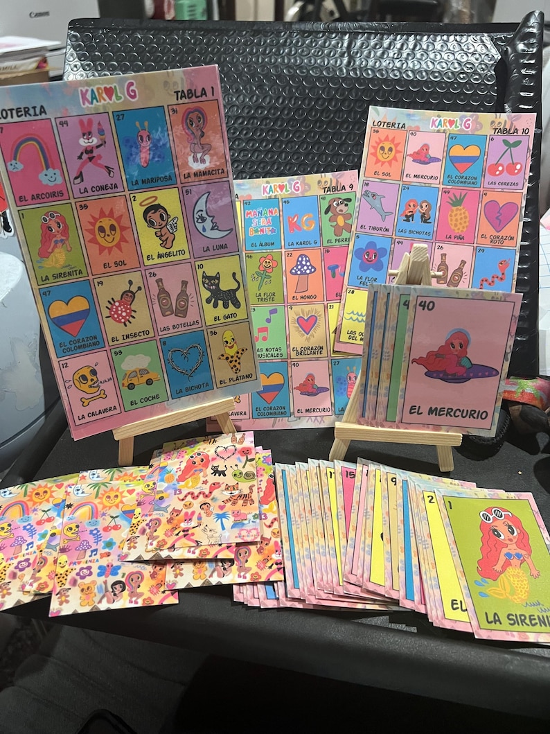 May include: A set of colorful playing cards with illustrations of various characters and objects. The cards are arranged in a grid pattern and feature the text "KAROL G" and "LOTERIA".