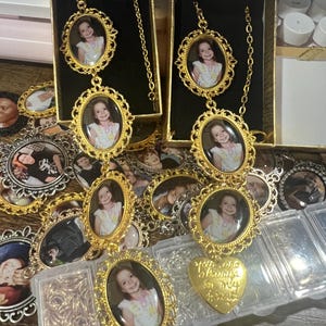 May include: Gold-tone necklaces with oval-shaped photo charms featuring a young girl. Each necklace has a heart-shaped charm with the text "We are always in my heart".