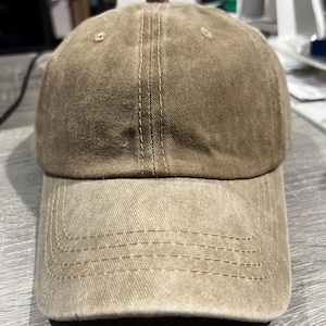 May include: A brown baseball cap with a distressed look. The cap has a curved brim and a stitched seam down the center of the crown.