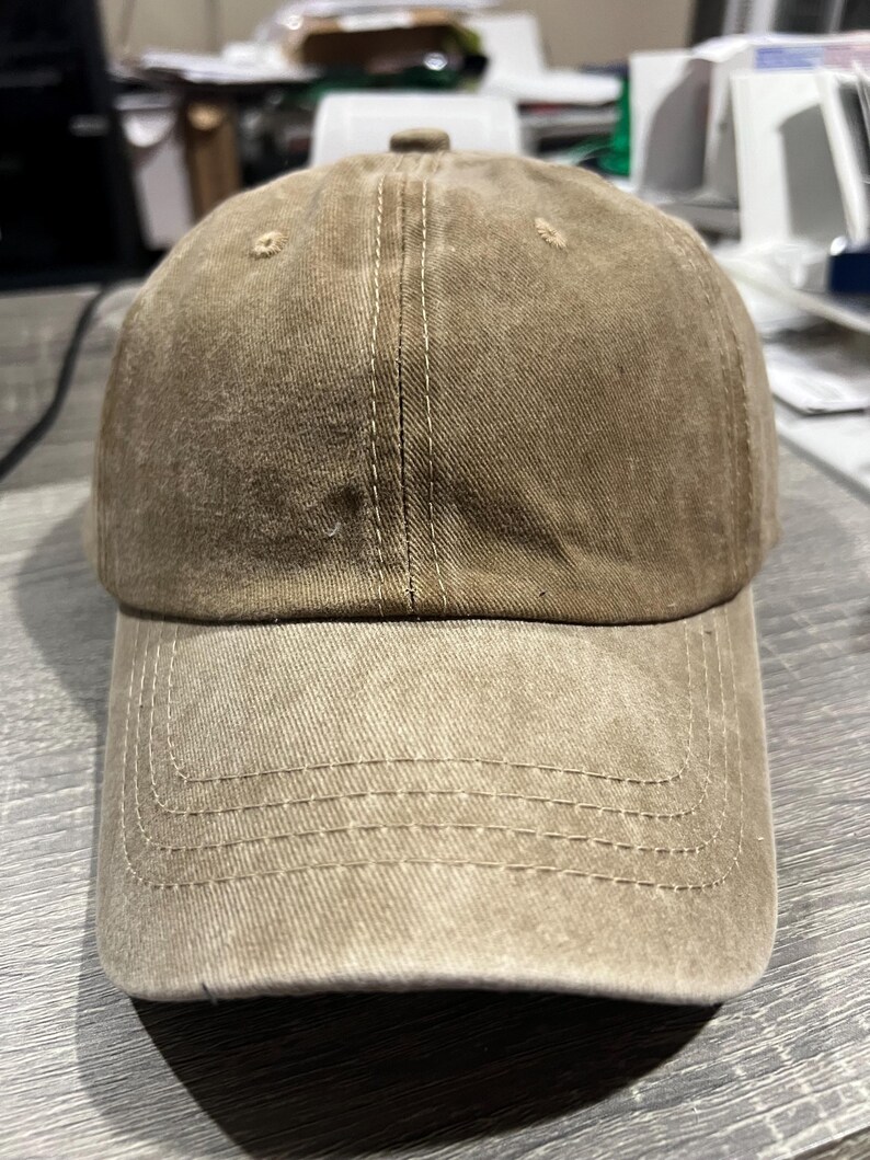 May include: A brown baseball cap with a distressed look. The cap has a curved brim and a stitched seam down the center of the crown.