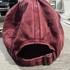 May include: A burgundy cotton baseball cap with an adjustable strap and buckle closure.