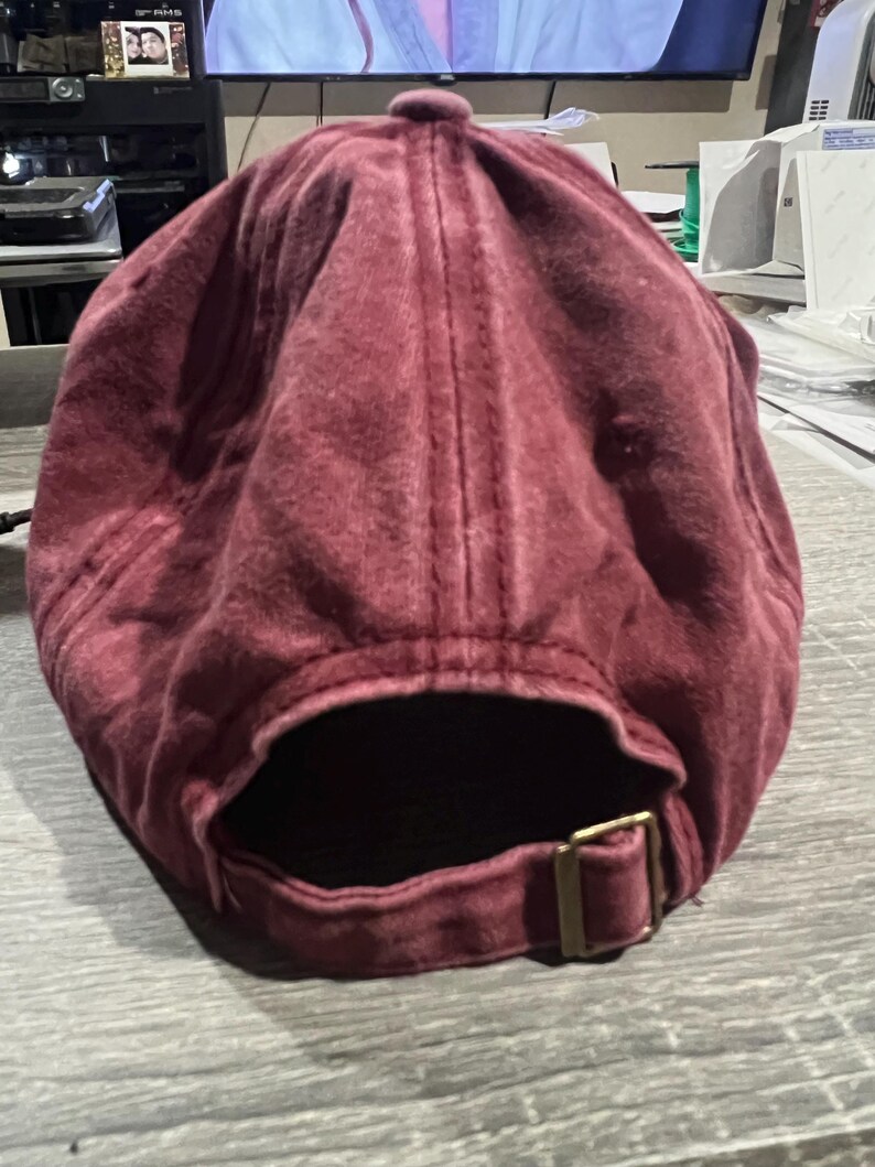 May include: A burgundy cotton baseball cap with an adjustable strap and buckle closure.