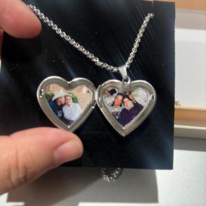 May include: Silver heart-shaped locket necklace with a chain. The locket opens to reveal two photos of a family.