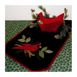 Może przedstawiać: Czarny bieżnik stołowy z filcu z wzorem czerwonego kardynała. Bieżnik ma czerwoną obwódkę i przedstawia małego, czerwonego kardynała w gnieździe na górze bieżnika.