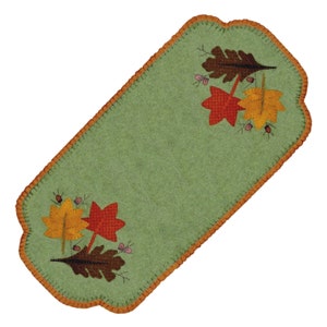 May include: A green felt table runner with an orange stitched border. The runner features an embroidered design of fall leaves in shades of red, orange, and brown.