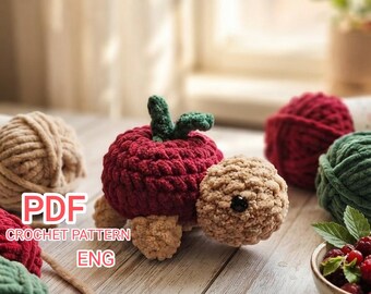 May include: A crochet turtle toy with a red apple-shaped shell featuring green leaves, a tan head with a black eye, and tan feet. The text PDF CROCHET PATTERN ENG is visible on the left. Several balls of yarn and a bowl of berries are nearby.