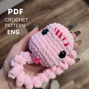 May include: A handmade pink crochet snake toy with black eyes and red accents. The plush toy is held in a hand. Text on the image reads "PDF CROCHET PATTERN ENG".