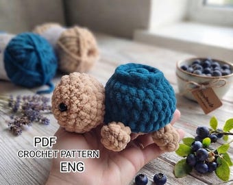 May include: A small, handmade crochet turtle toy featuring a beige head and limbs with a dark teal shell. The text PDF CROCHET PATTERN ENG is visible on the left side. The turtle is crafted from soft, textured yarn and has a black bead eye.
