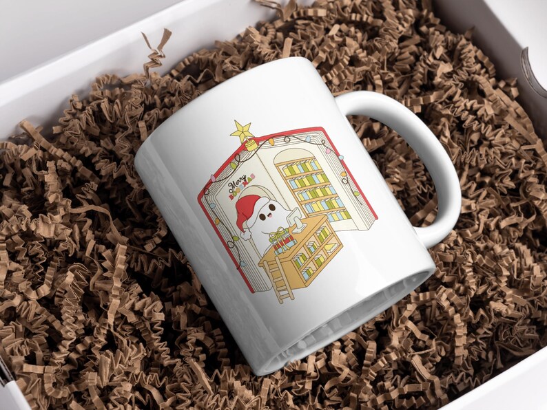 May include: White ceramic mug with a Christmas-themed illustration. The design features a cartoon ghost wearing a Santa hat, inside a book with a library scene. The mug is in a white box with brown paper filler. The text "Merry Xmas" is visible.