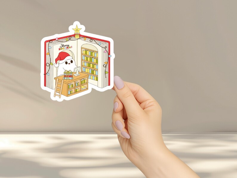 May include: A sticker featuring a cartoon ghost wearing a Santa hat, inside a book-shaped library. The ghost is at a desk with presents, and the library has bookshelves and Christmas lights. The text "Merry Bookmas" is visible.