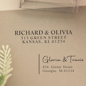 Puede incluir: Un sello transparente con el texto "COLOP" se utiliza para imprimir una dirección en un sobre marrón claro. La dirección impresa dice "RICHARD & OLIVIA" y "Gloria & Travis" con sus respectivas direcciones. El sobre está sobre una superficie marrón claro.