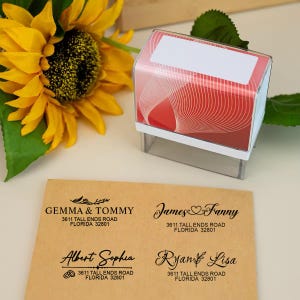 Puede incluir: Un sello de dirección transparente con un diseño rojo y blanco, junto a cuatro ejemplos de direcciones en papel marrón. Una brillante flor de girasol amarilla está en el fondo. Los ejemplos de direcciones incluyen nombres y direcciones.