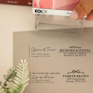 Puede incluir: Un sello transparente con la marca "COLOP" se utiliza para imprimir direcciones en un sobre marrón claro. El sobre tiene cuatro diseños de direcciones diferentes, con nombres y direcciones.