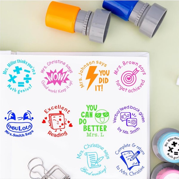 May include: A collection of colorful teacher stamps with various positive messages and designs. Stamps include phrases like "Math genius!", "WOW!", "YOU DID IT!", and "Excellent Reading". The stamps are in blue, pink, orange, and green.