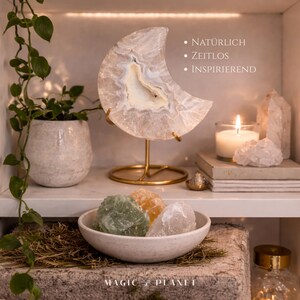 K&ouml;nnte beinhalten: Eine dekorative Regal-Anordnung mit einer halbmondf&ouml;rmigen Achatlampe mit goldenem St&auml;nder, einer brennenden Kerze und einer Schale mit farbigen Kristallen. Der Text auf dem Bild lautet "NAT&Uuml;RLICH", "ZEITLOS" und "INSPIRIEREND". Der untere Teil des Bildes lautet "MAGIC + PLANET".