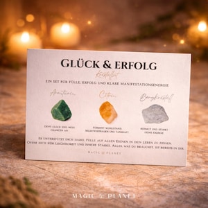 K&ouml;nnte beinhalten: Eine Karte mit dem deutschen Text "GL&Uuml;CK & ERFOLG" und drei Kristallen: Aventurin (gr&uuml;n), Citrin (orange) und Bergkristell (grau). Die Karte enth&auml;lt Text &uuml;ber die Eigenschaften der Kristalle und die Marke "MAGIC PLANET".