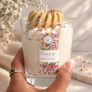 Könnte beinhalten: Eine Kerze im Klarglas mit weißer Wachsbasis, gekrönt von einem beigen, bundt-kuchenförmigen Wachsstück und weißem Sprühwachs, verziert mit bunten Streuseln. Das Etikett zeigt Magic Planet, happy BIRTHDAY, 40 hours und 230 g.